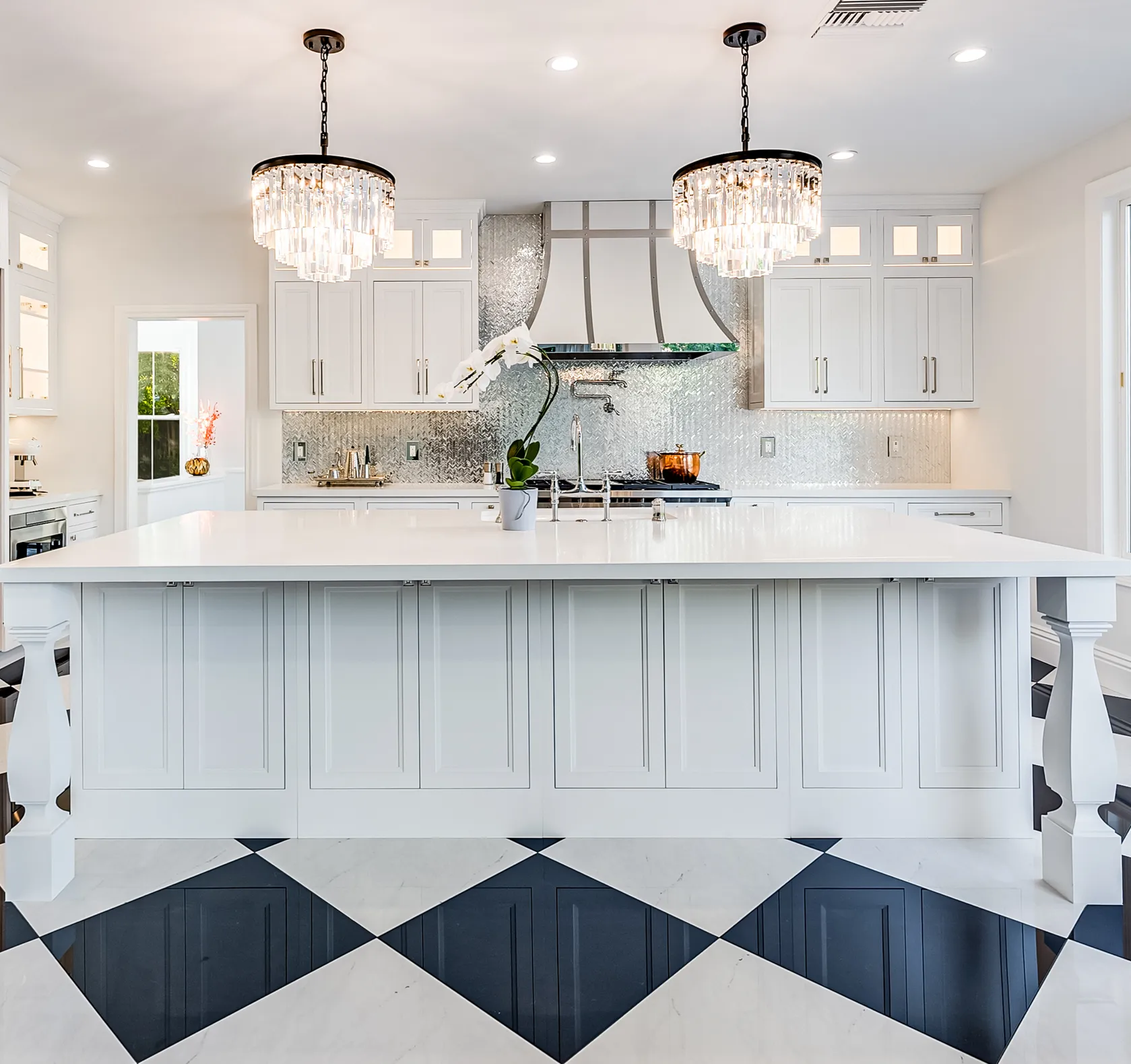 White kitchen island under two crystal chandeliers with checkerboard marble floor in Calabasas