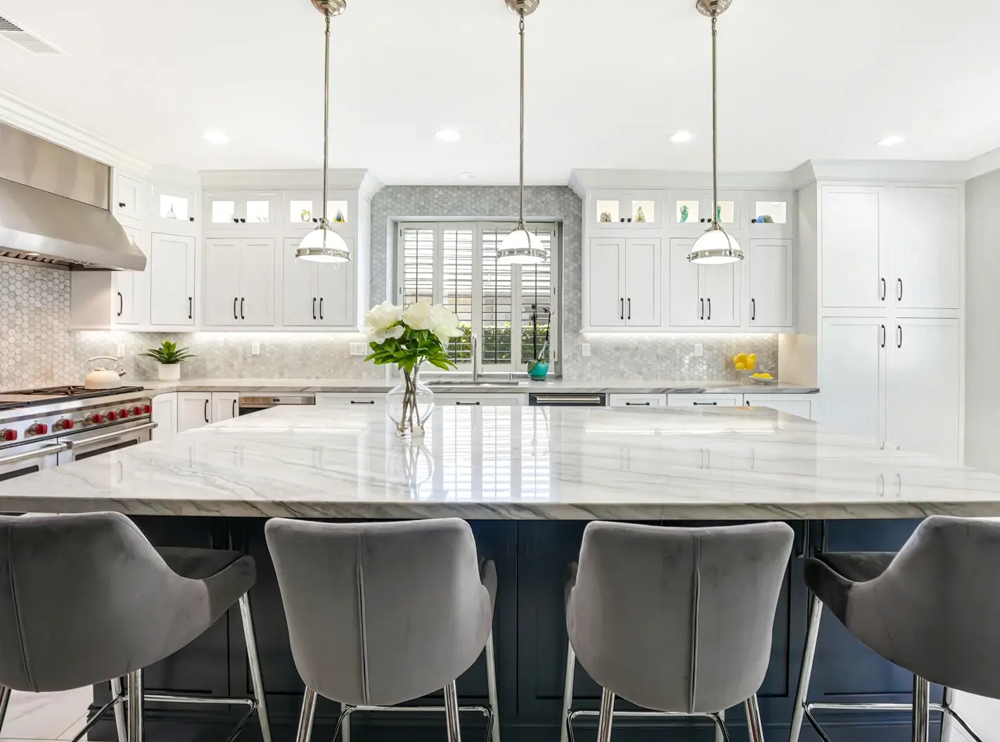 Navy kitchen island with quartz top, gray stools and chrome pendants