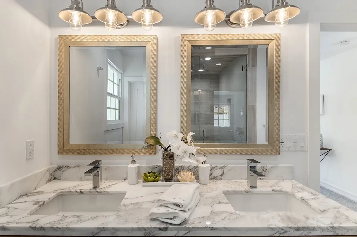 Double vanity with marble counter, brass-framed mirrors and sconces