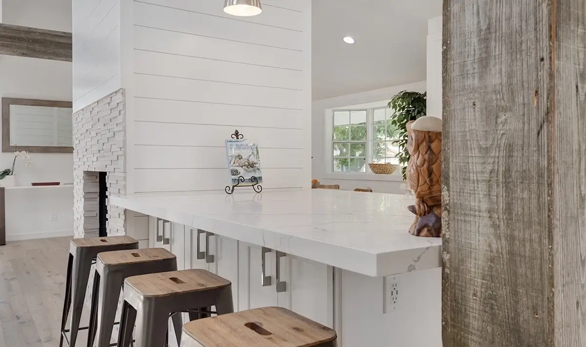 Kitchen island with marble top and metal stools beside a stone fireplace