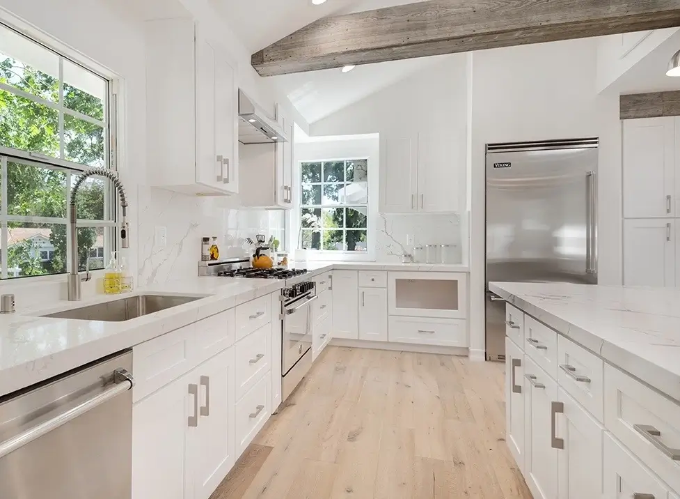 White Shaker kitchen with marble counters, farmhouse faucet and reclaimed-wood beam