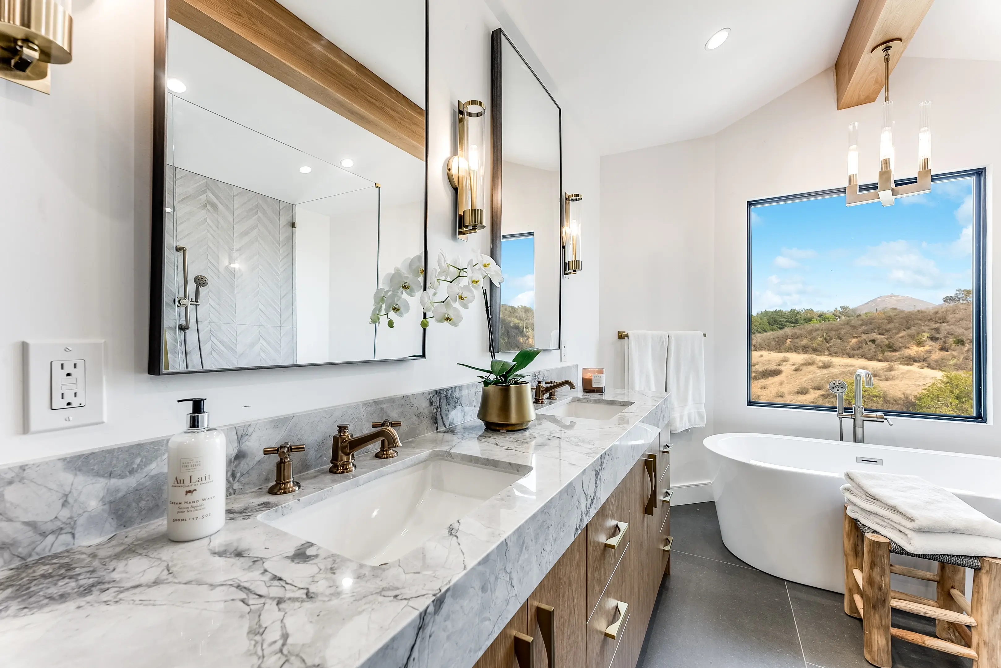 Walnut floating vanity with marble top and freestanding tub beyond