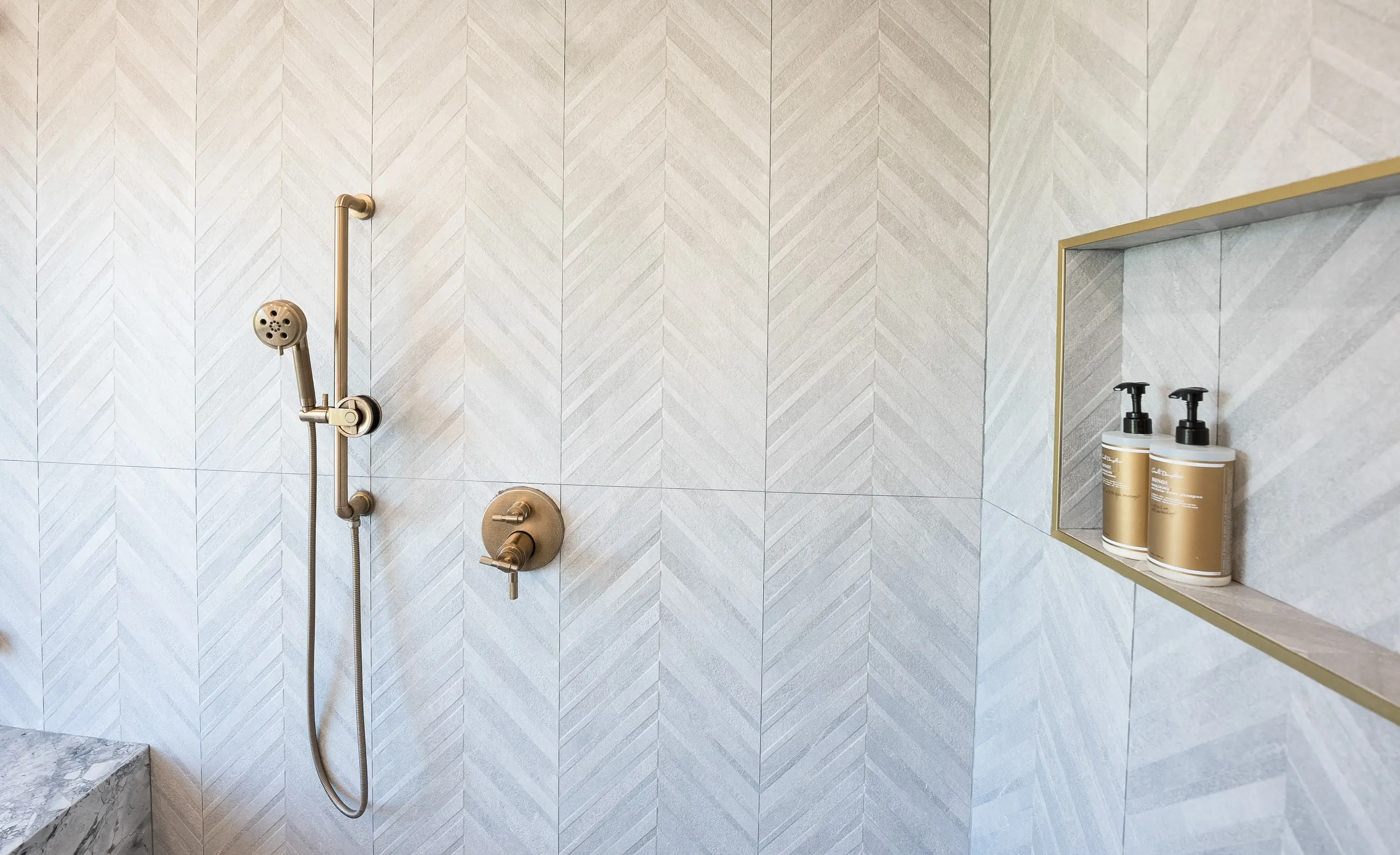 Herringbone marble shower with brass fixtures and niche