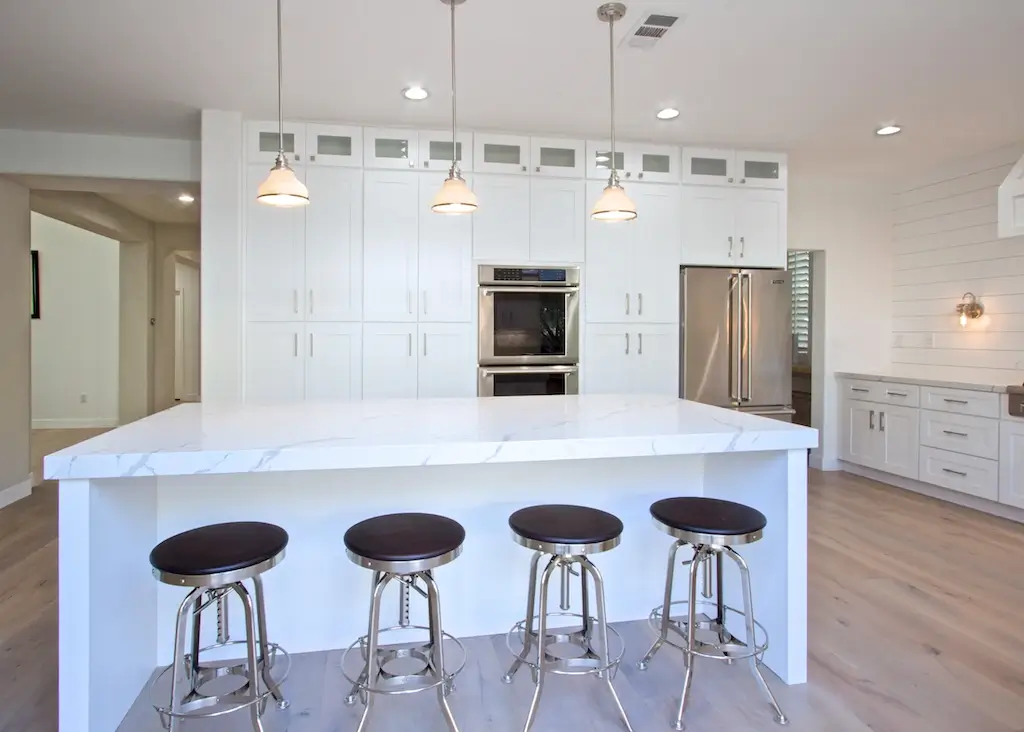 Marble island with four black stools and glass-front upper cabinets