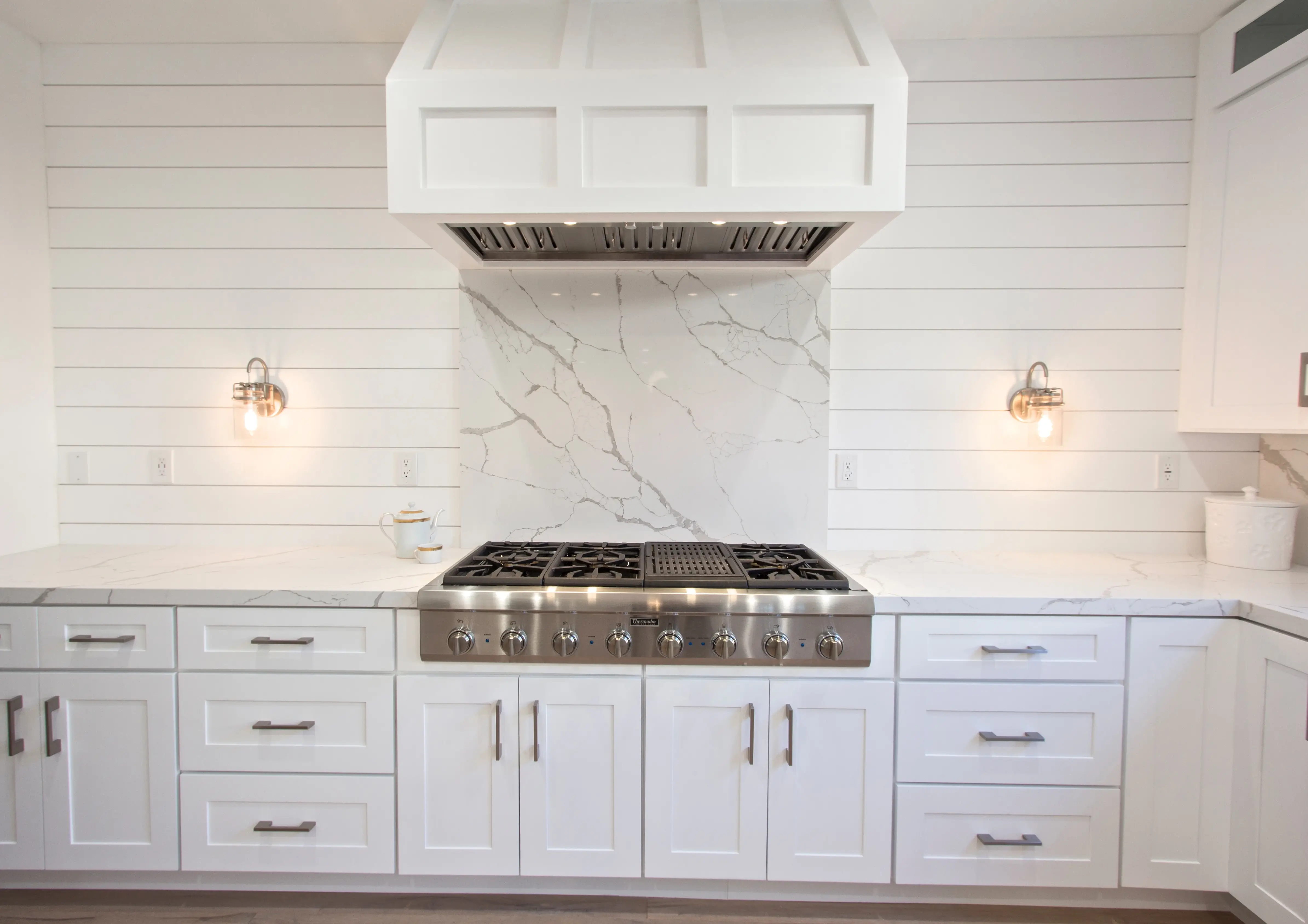 Shiplap range wall with custom hood, marble backsplash and brass sconces