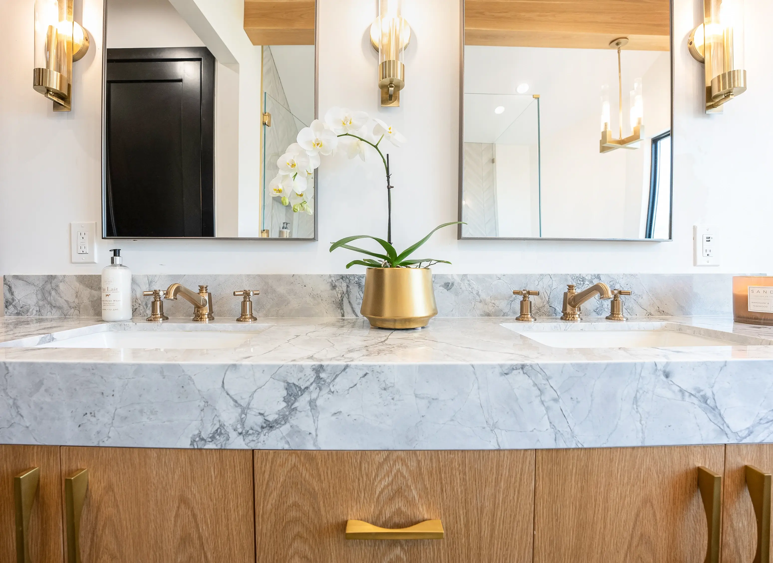 Marble vanity with brass faucets and backlit mirrors