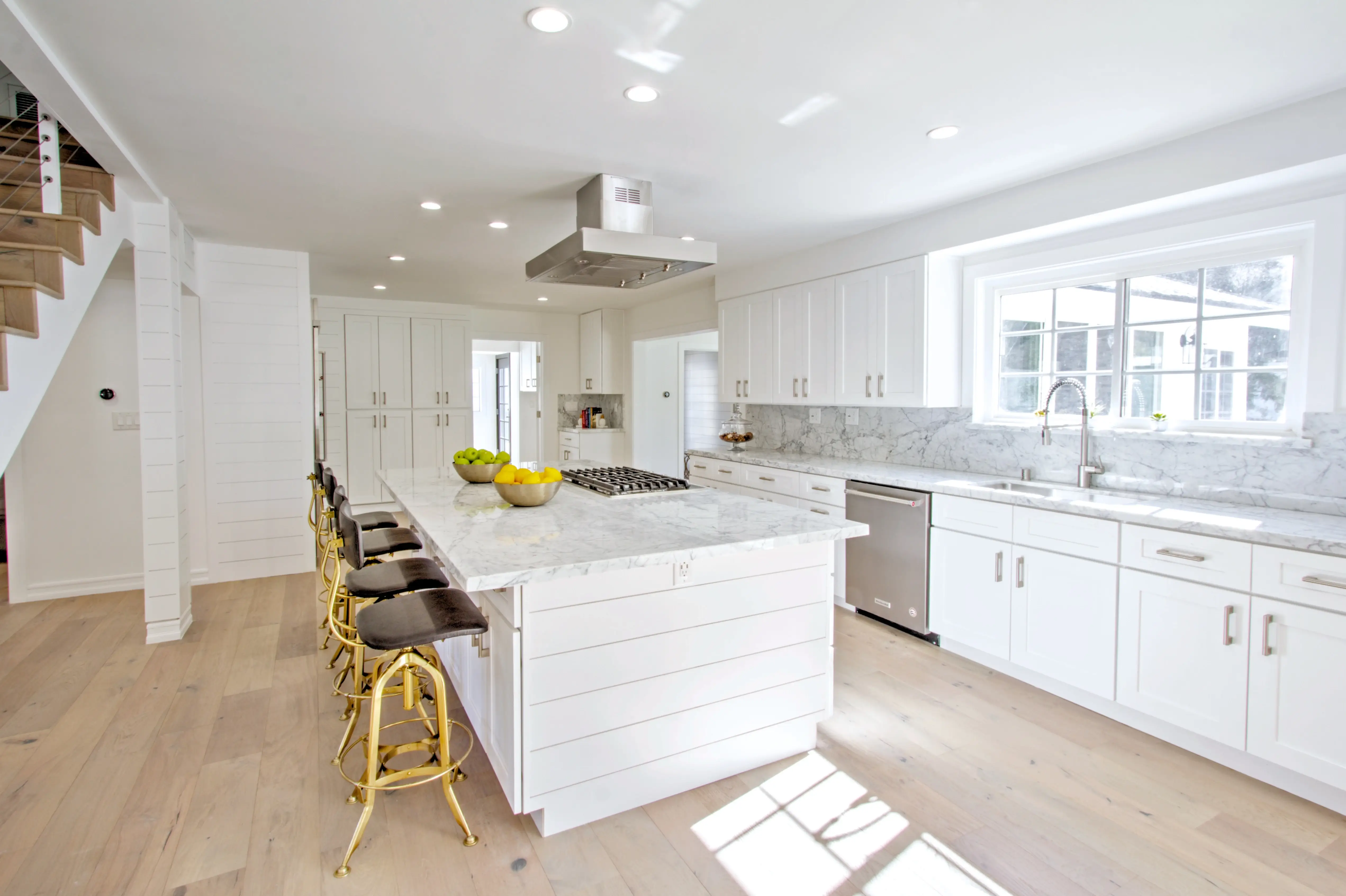 Kitchen island with five brass stools and white Shaker cabinets