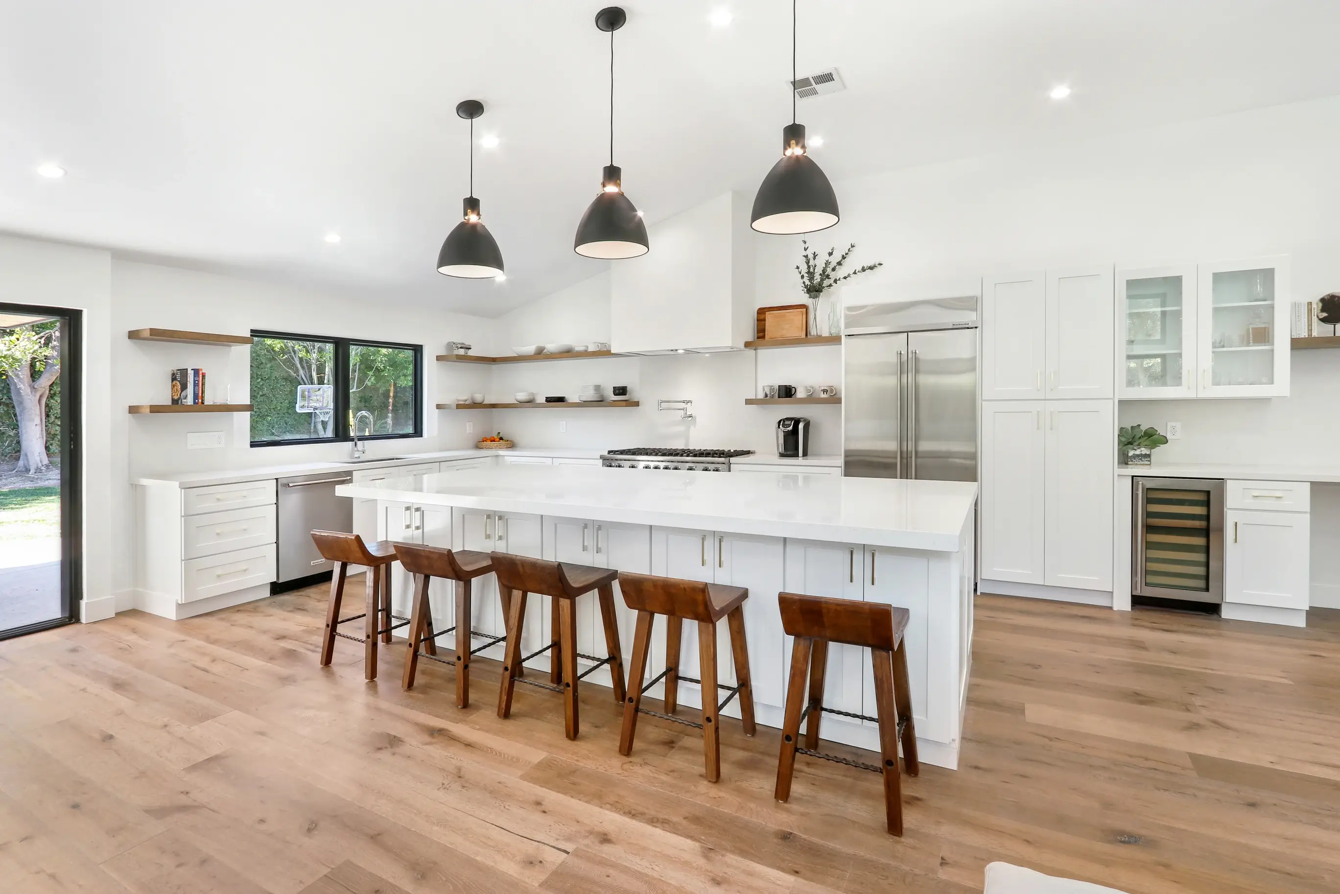 Open kitchen with long white island, oak floating shelves and black pendants
